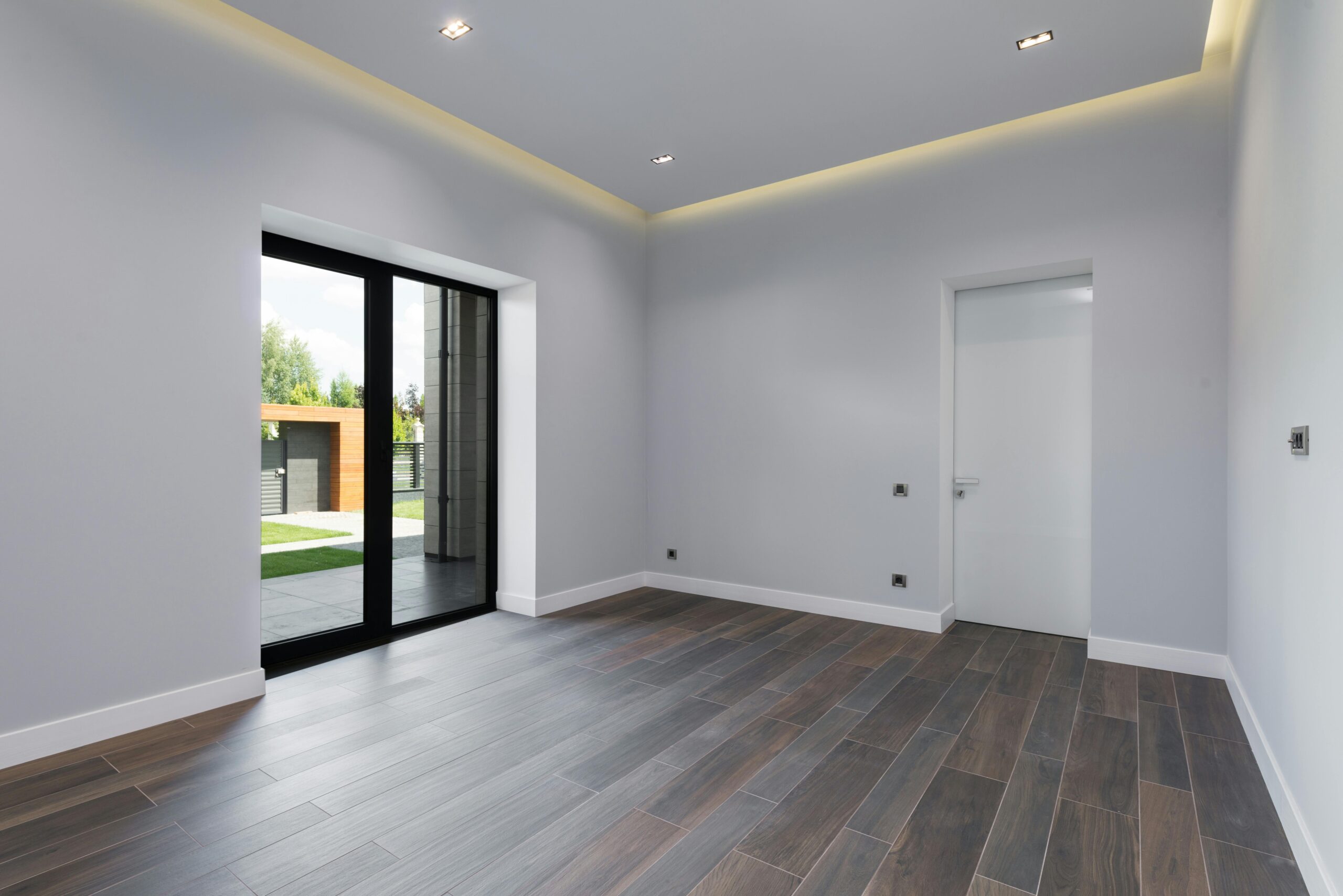 Projects Spacious and modern empty room with wooden floors and large windows overlooking a garden.